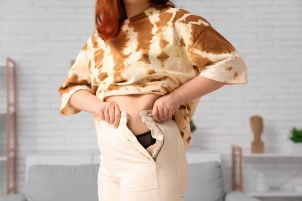 Image of woman trying to do her trousers up after pregnancy weight gain Calton